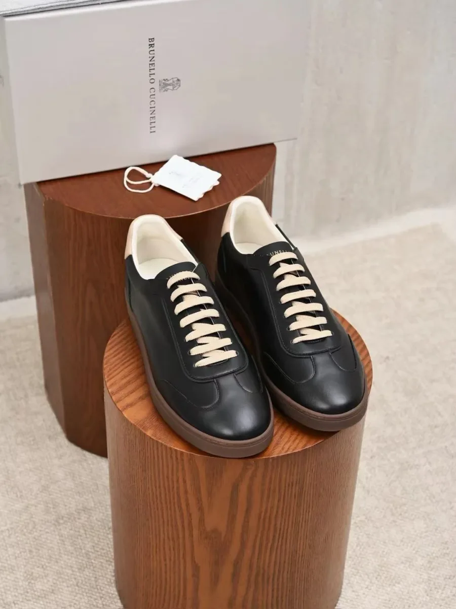 Пара чёрных кожаных кроссовок Brunello Cucinelli спереди, с белыми шнурками и светлой окантовкой