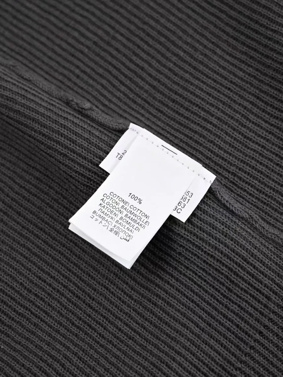 Серое поло крупным планом с пуговицами, рельефной фактурой вязки и внутренними бирками