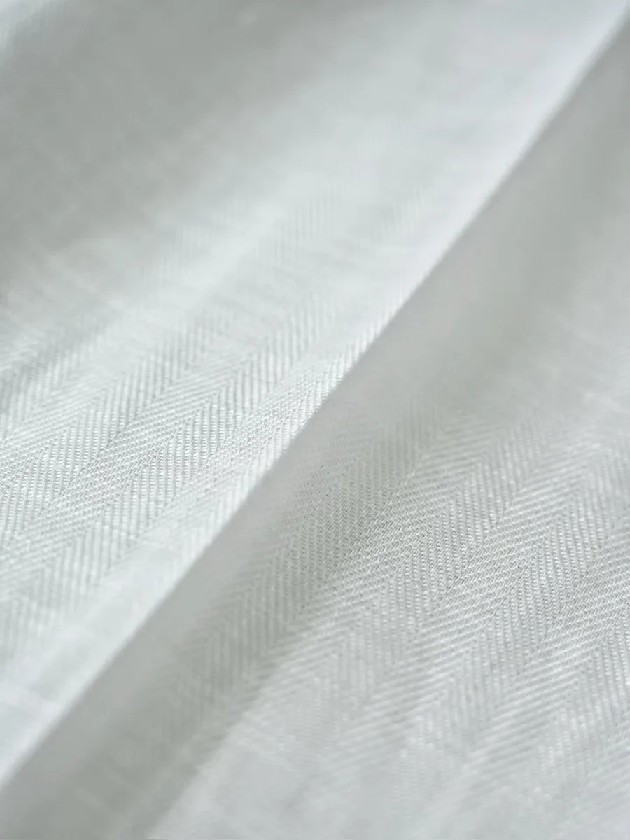 Белая льняная ткань брюк Loro Piana крупным планом, заметное диагональное плетение материала
