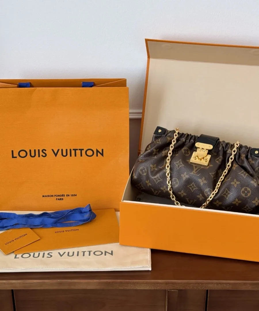 Сумка Louis Vuitton Pochette S-Lock рядом с фирменной коробкой и пакетом
