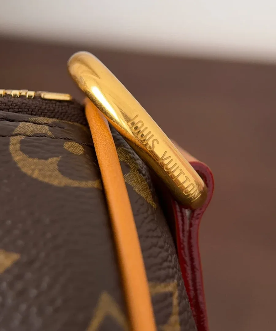 Золотистое полукольцо на боковой части сумки с гравировкой Louis Vuitton