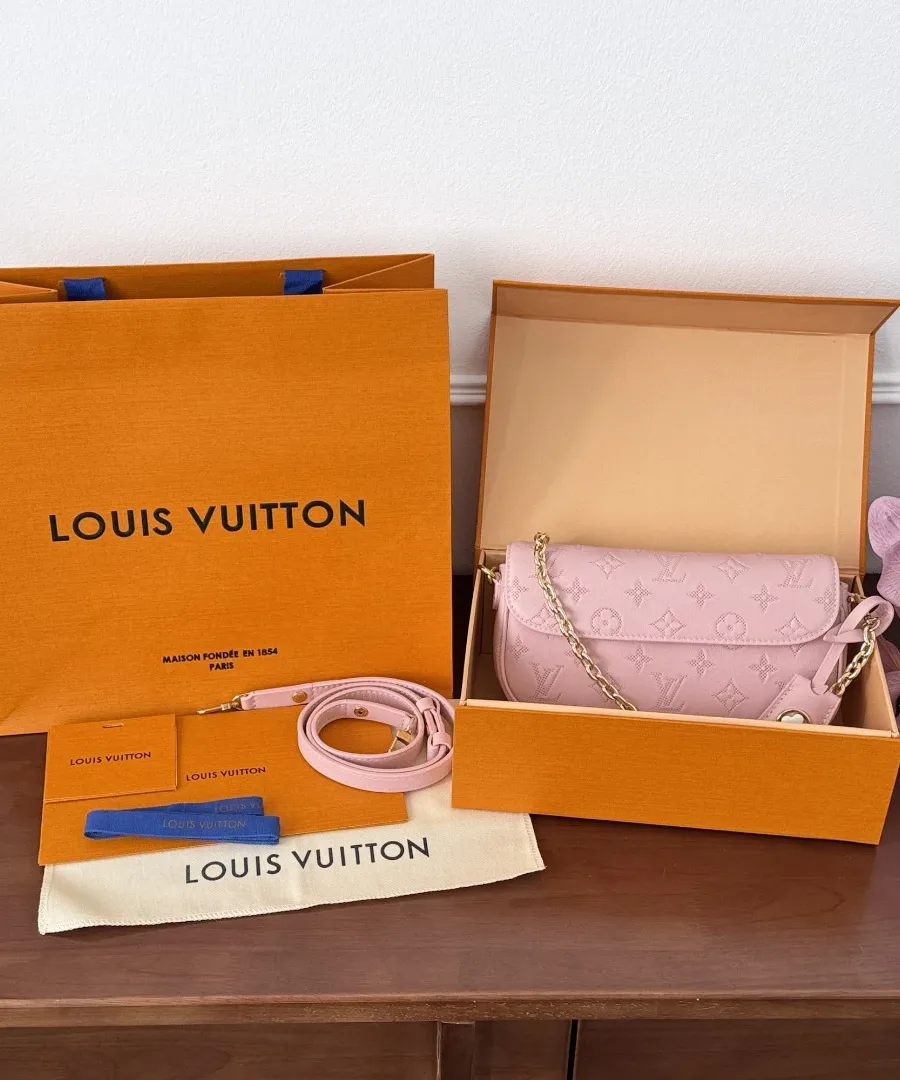 Фирменная упаковка Louis Vuitton: оранжевая коробка, пакет и пыльник рядом с розовой сумкой