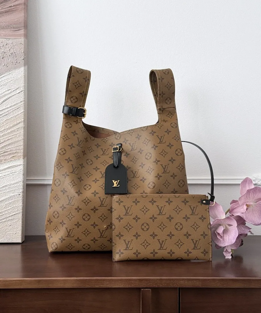 Коричневая сумка Louis Vuitton Atlantis GM с косметичкой на деревянном столе, вид спереди.