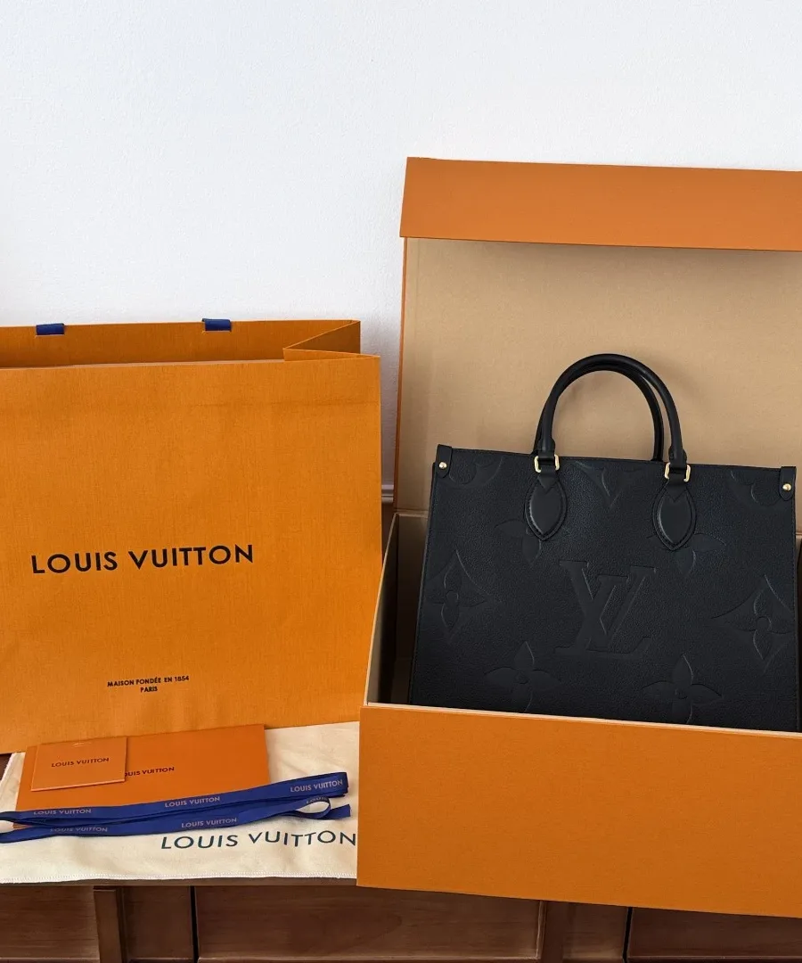 Черная сумка-тоут Louis Vuitton OnTheGo MM рядом с фирменной оранжевой коробкой и пакетом
