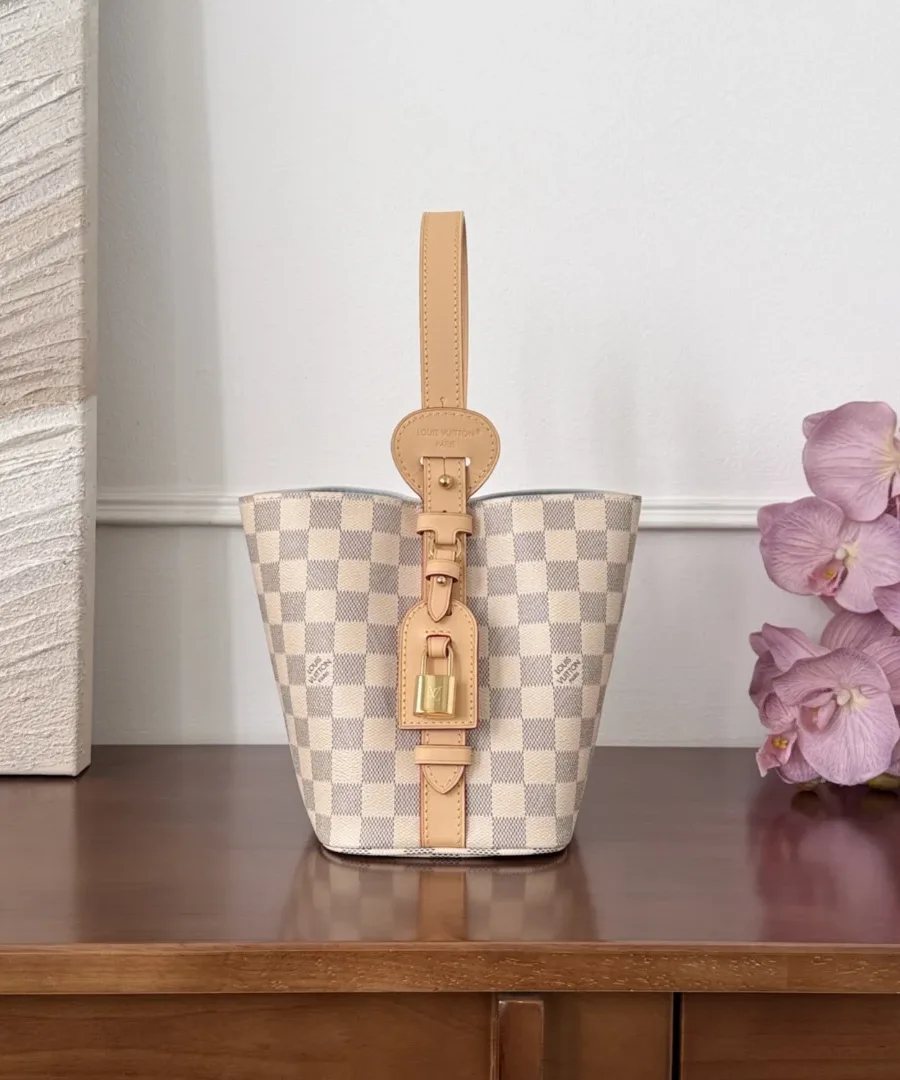 Сумка-ведро Louis Vuitton All-In BB, вид сбоку, демонстрирующий кожаный ремешок с замком.