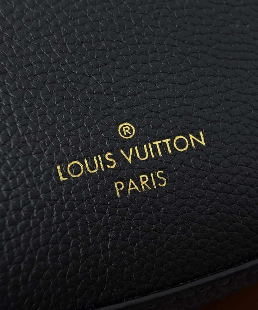 Крупный план золотистого тиснения Louis Vuitton Paris на чёрной зернистой коже