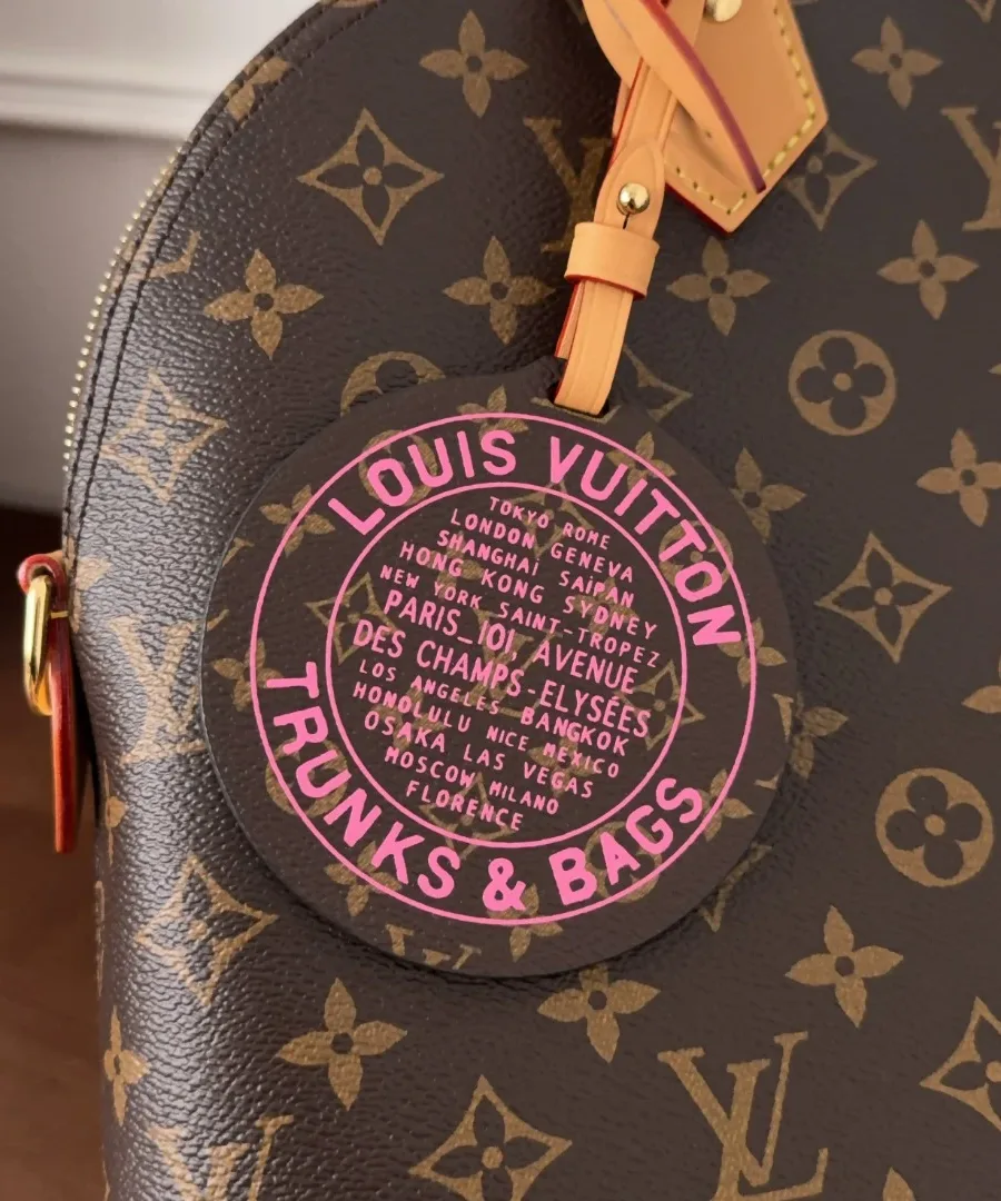Крупный план круглого розового брелока с надписью Louis Vuitton Trunks & Bags