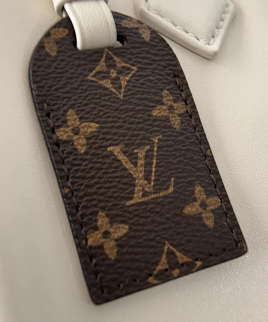 Крупный план съемной багажной бирки из коричневой канвы Monogram на бежевой сумке