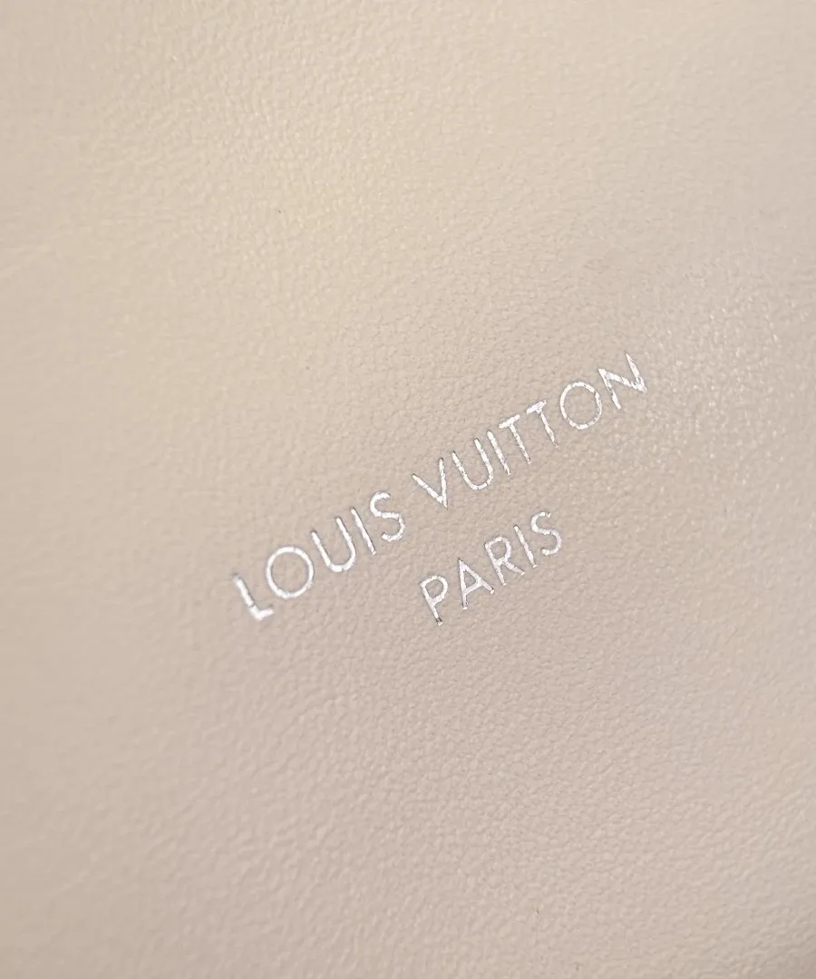 Крупный план тисненого серебристого логотипа Louis Vuitton Paris на бежевой коже