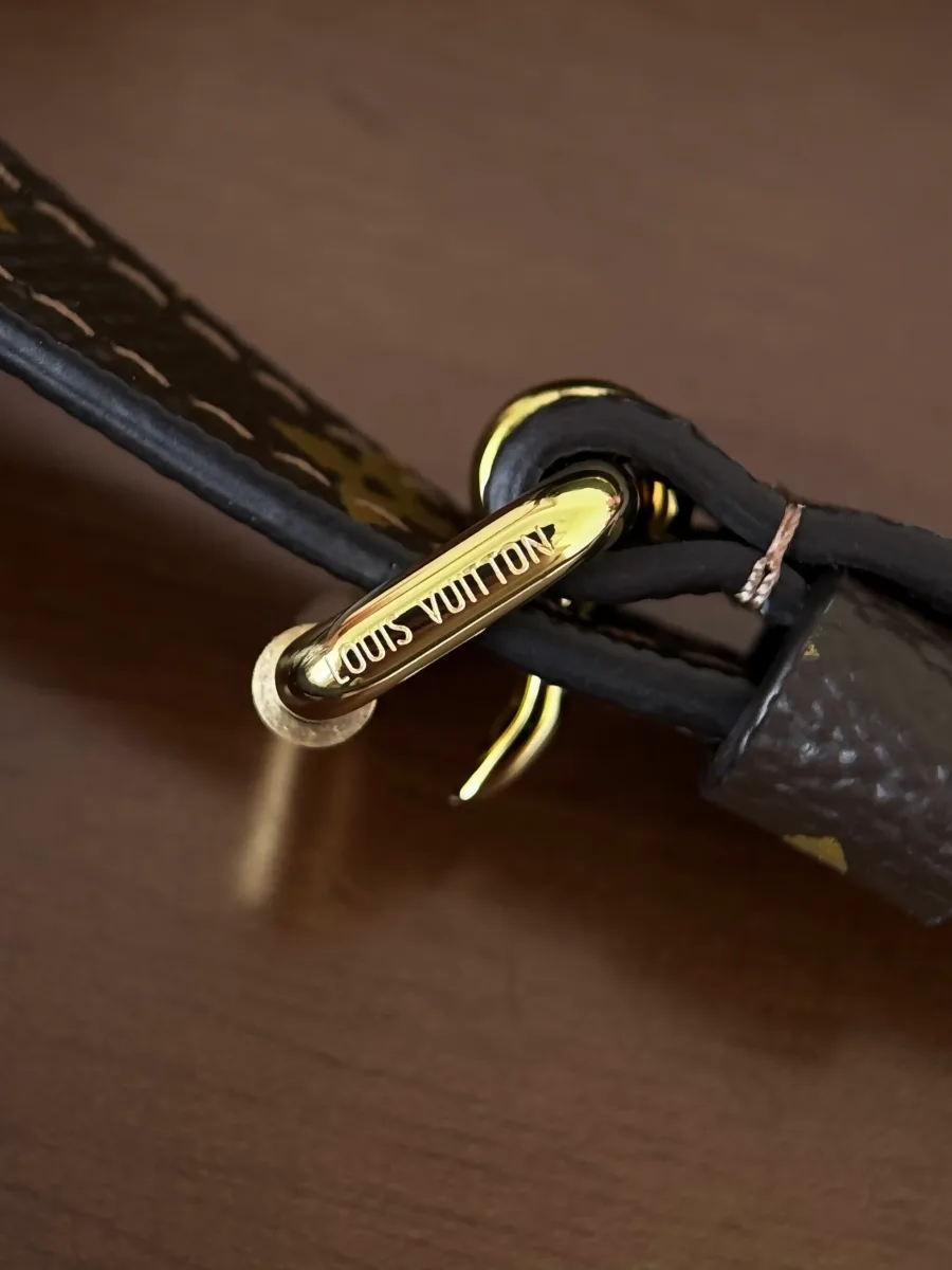 Крупный план золотистой пряжки ремня с надписью Louis Vuitton