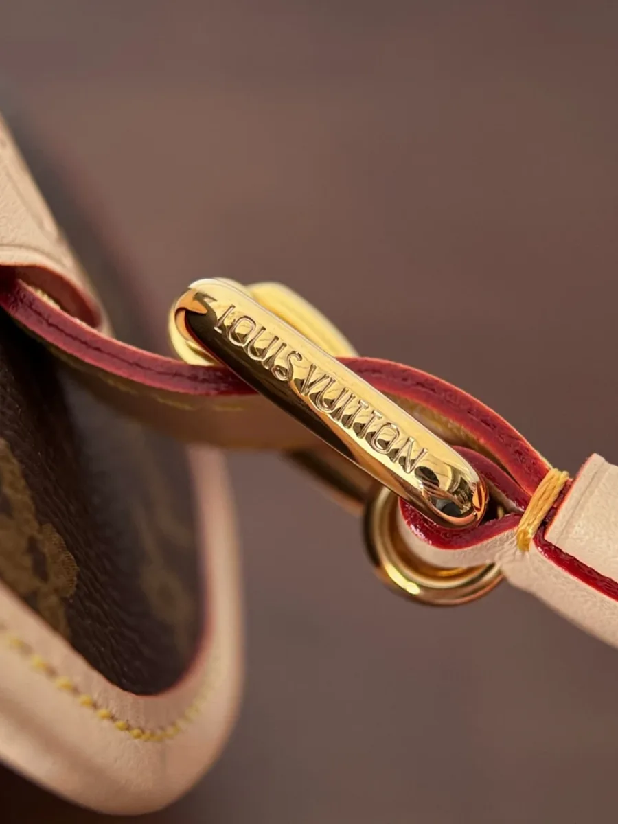Крупный план золотистого карабина с гравировкой Louis Vuitton на кожаном креплении