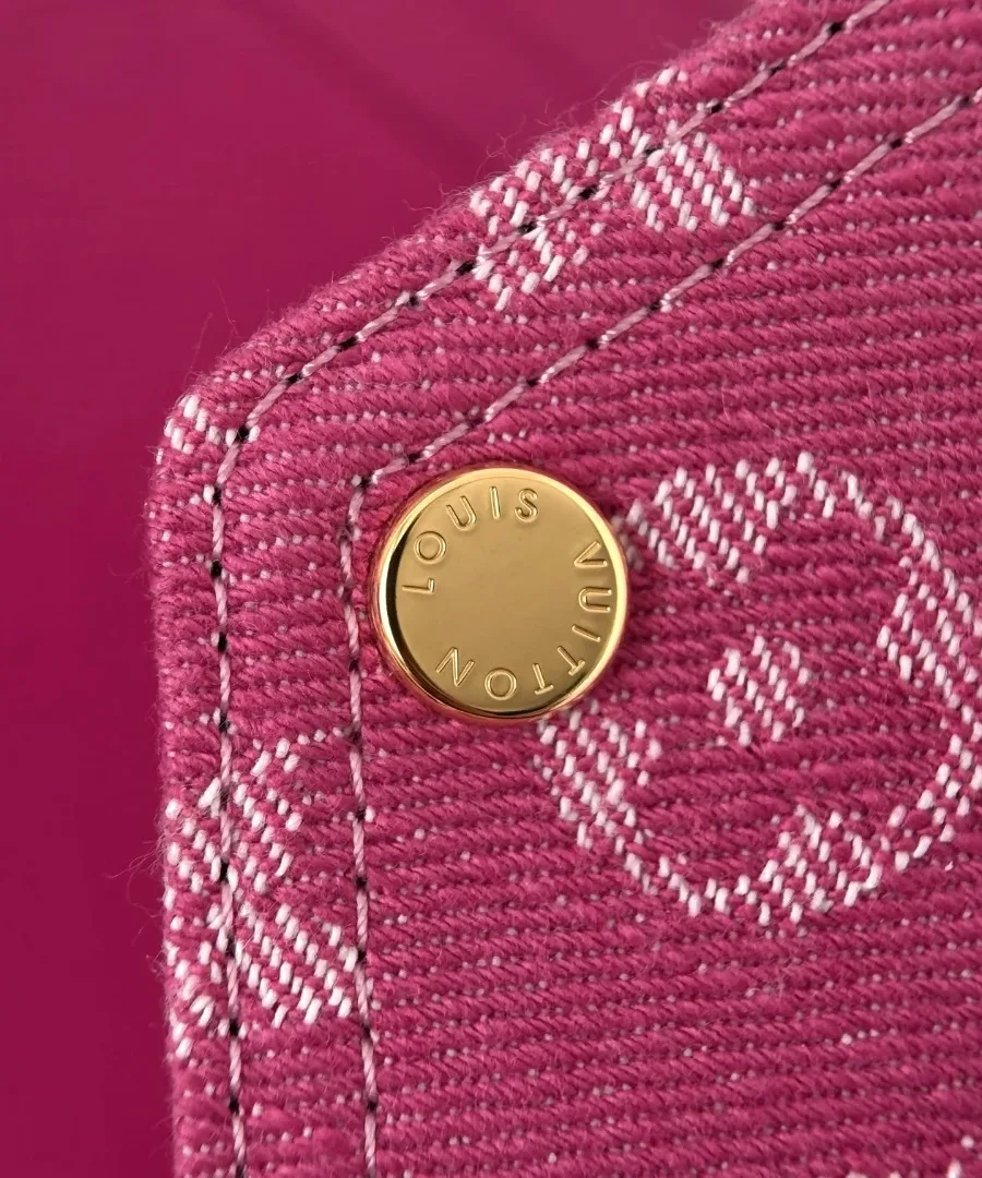 Крупный план золотистой кнопки с гравировкой Louis Vuitton на розовом дениме