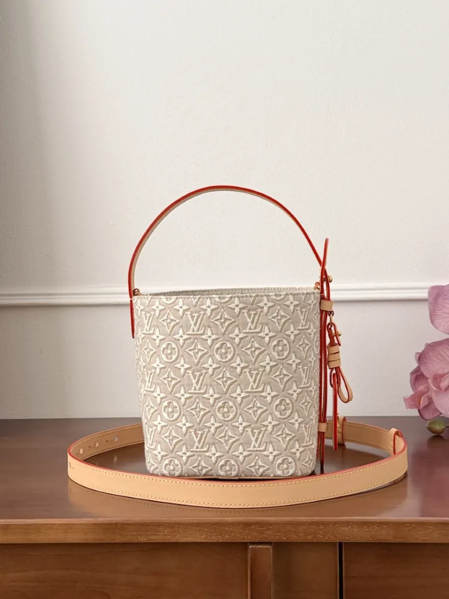 Бежевая сумка-ведро Louis Vuitton с плечевым ремнем на деревянном столе.