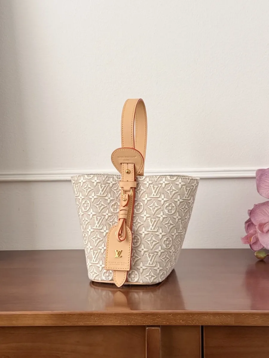 Вид сбоку на бежевую сумку-ведро Louis Vuitton с кожаной отделкой и биркой.