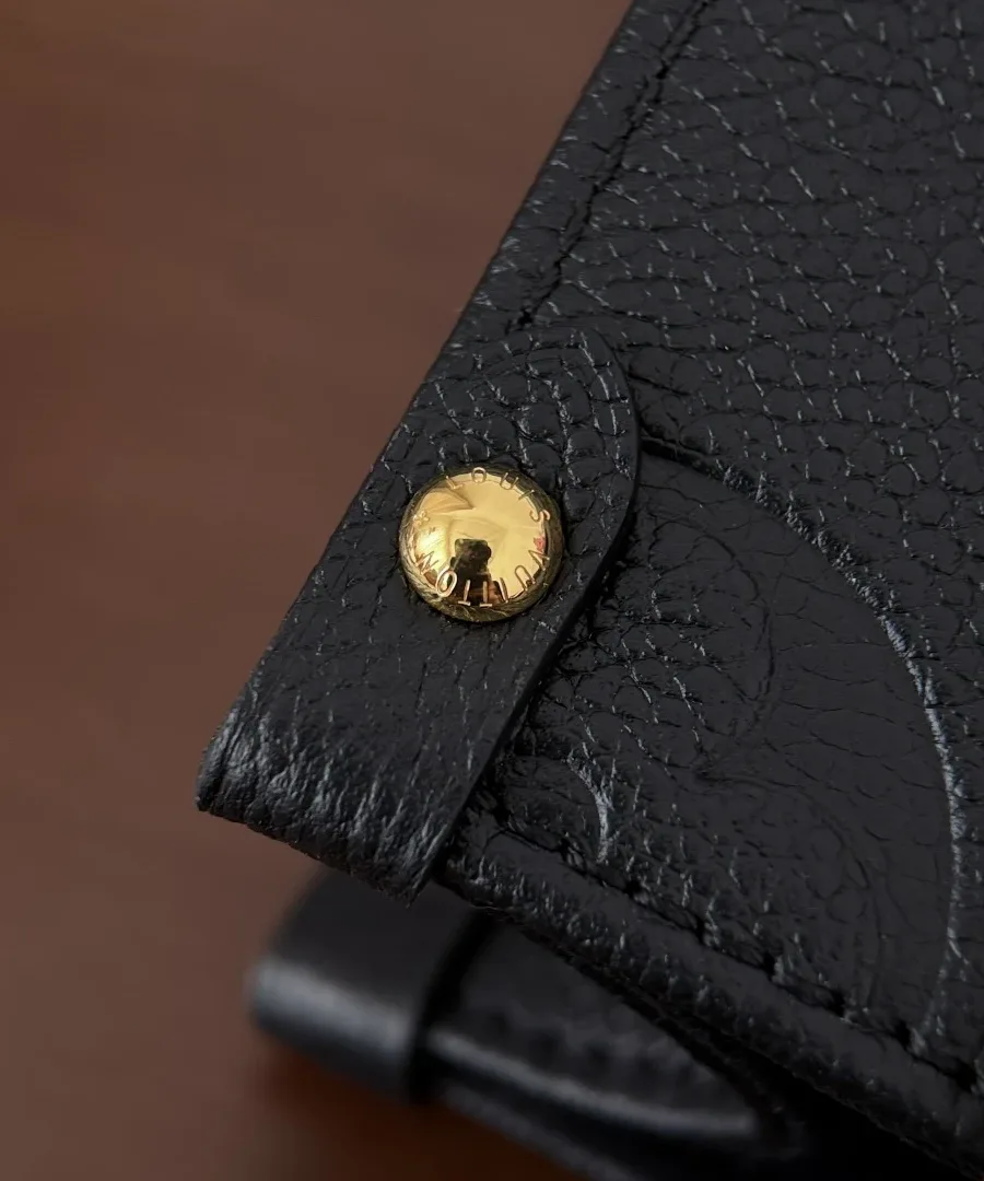 Деталь боковой кнопки золотистого цвета на черной кожаной сумке Louis Vuitton
