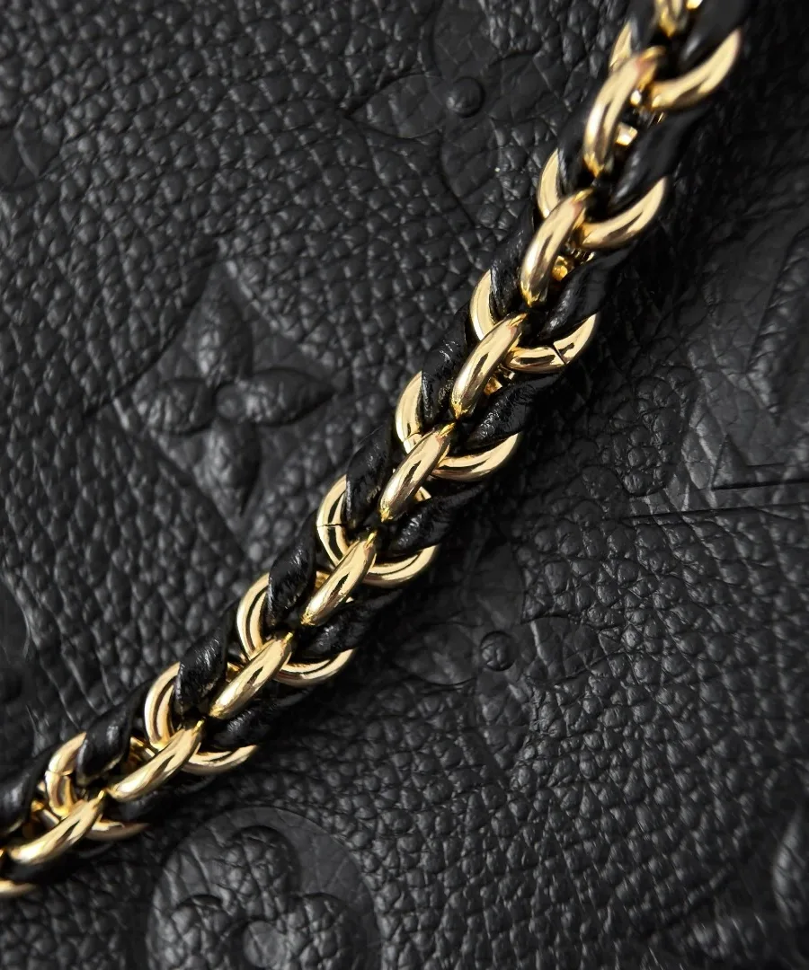 Крупный план тисненой кожи Monogram Empreinte и золотистой цепочки с кожаным плетением