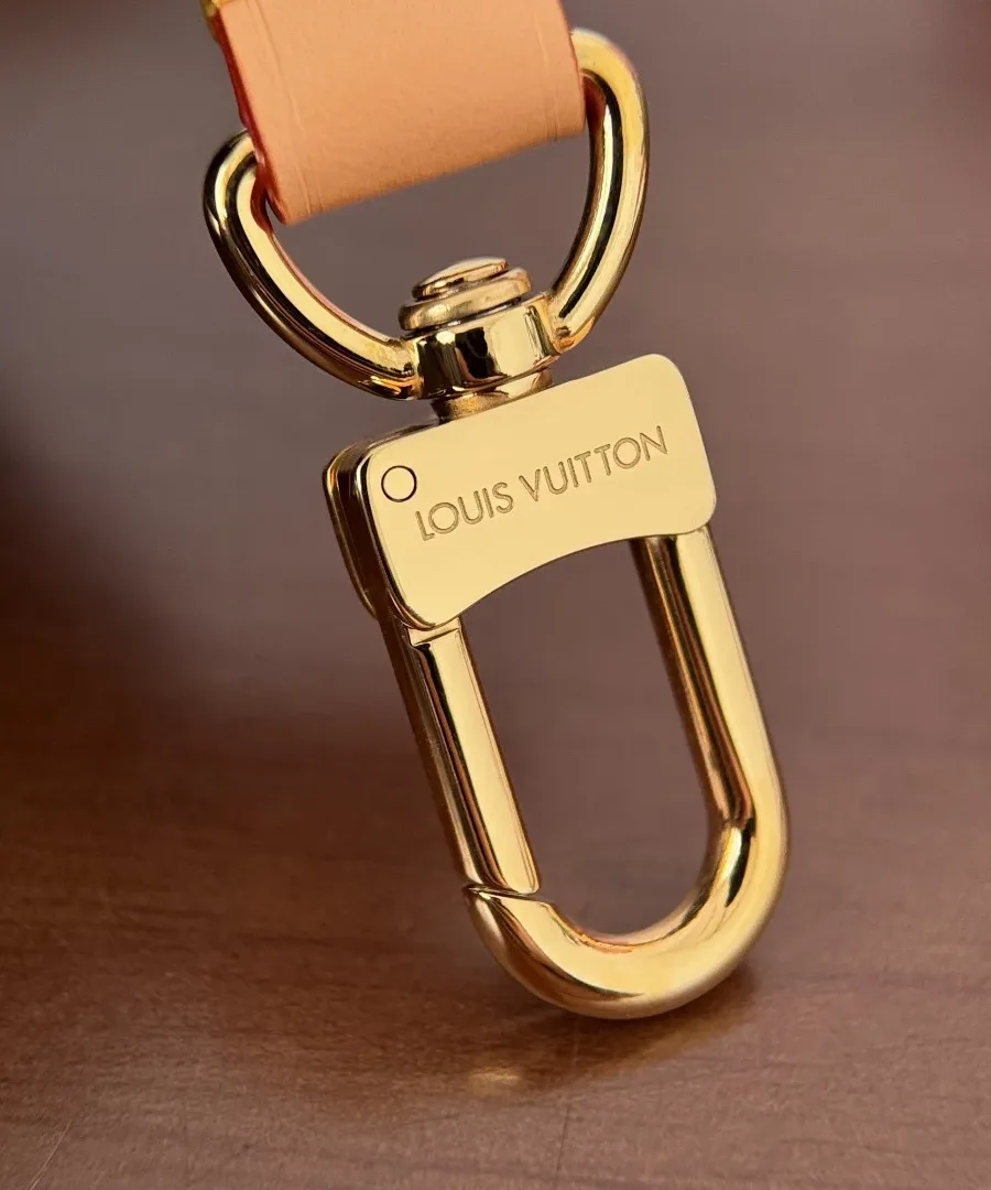 Крупный план золотистого карабина с гравировкой Louis Vuitton