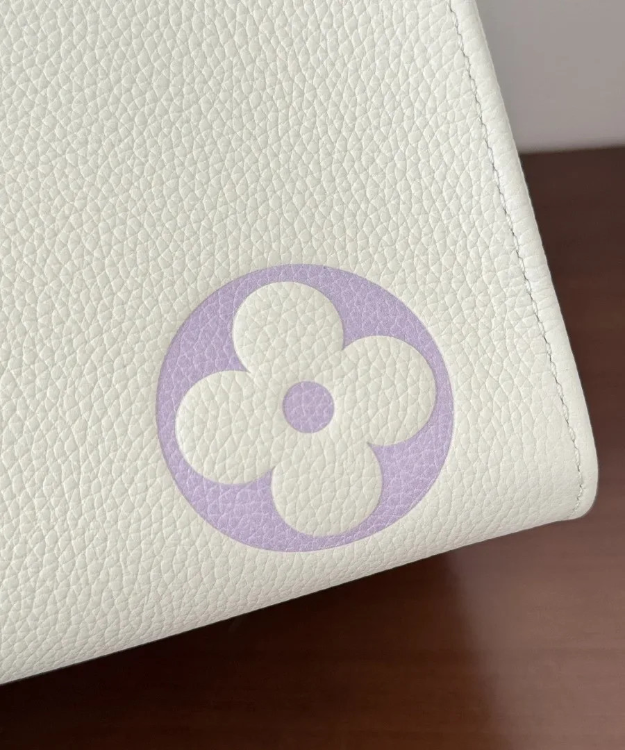 Крупный план угла сумки с сиреневым цветком Monogram на белой зернистой коже