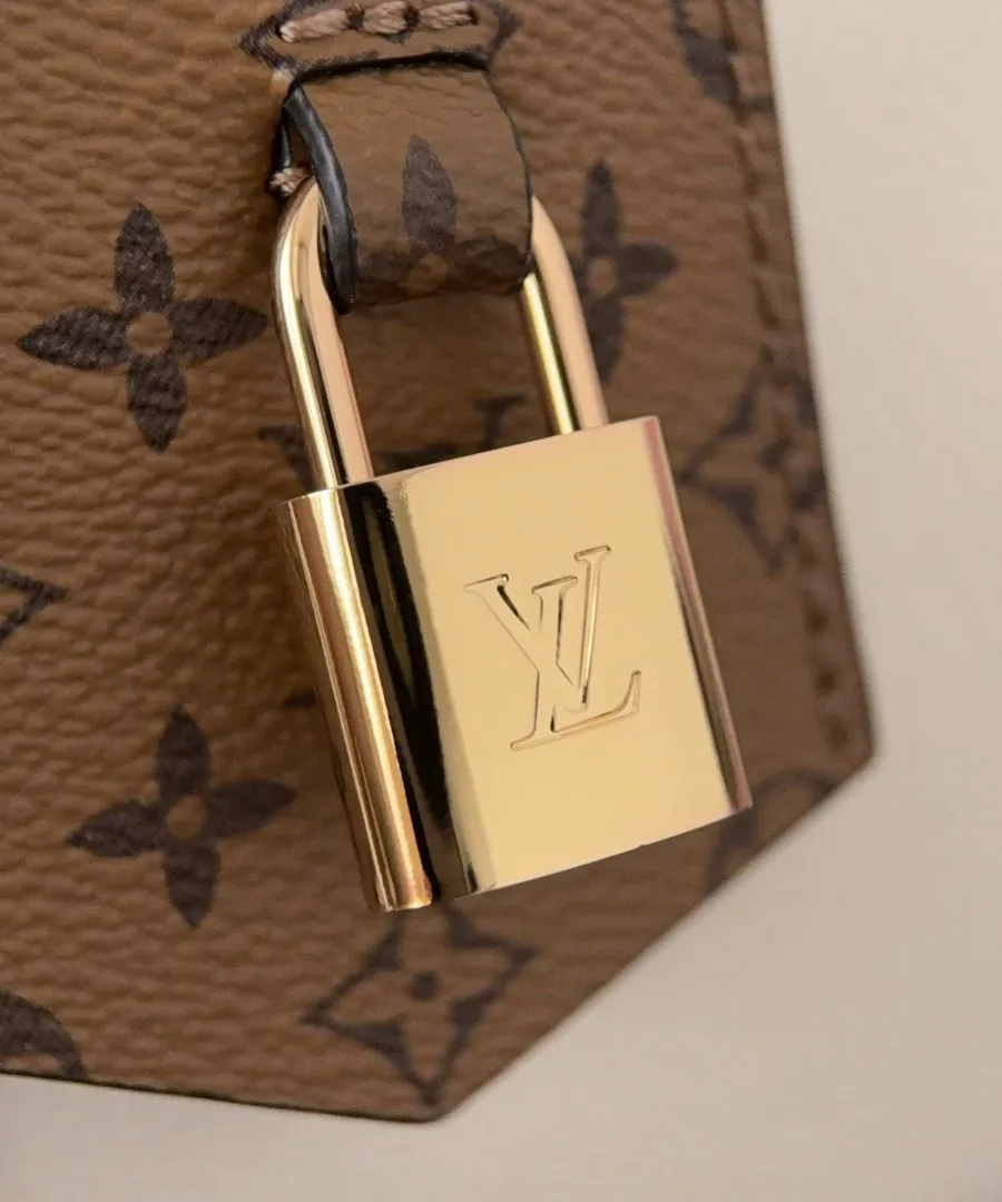 Золотистый металлический замок-падлок с логотипом LV на фоне канвы Monogram