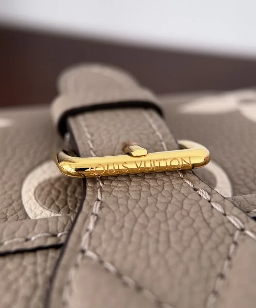 Крупный план золотистой пряжки с гравировкой Louis Vuitton на клапане сумки