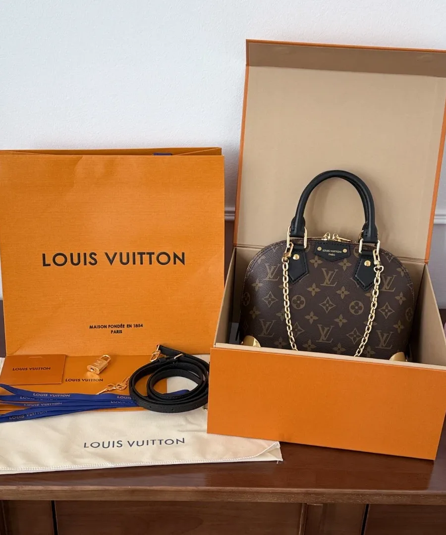 Сумка Louis Vuitton Alma BB рядом с фирменной оранжевой коробкой и пакетом