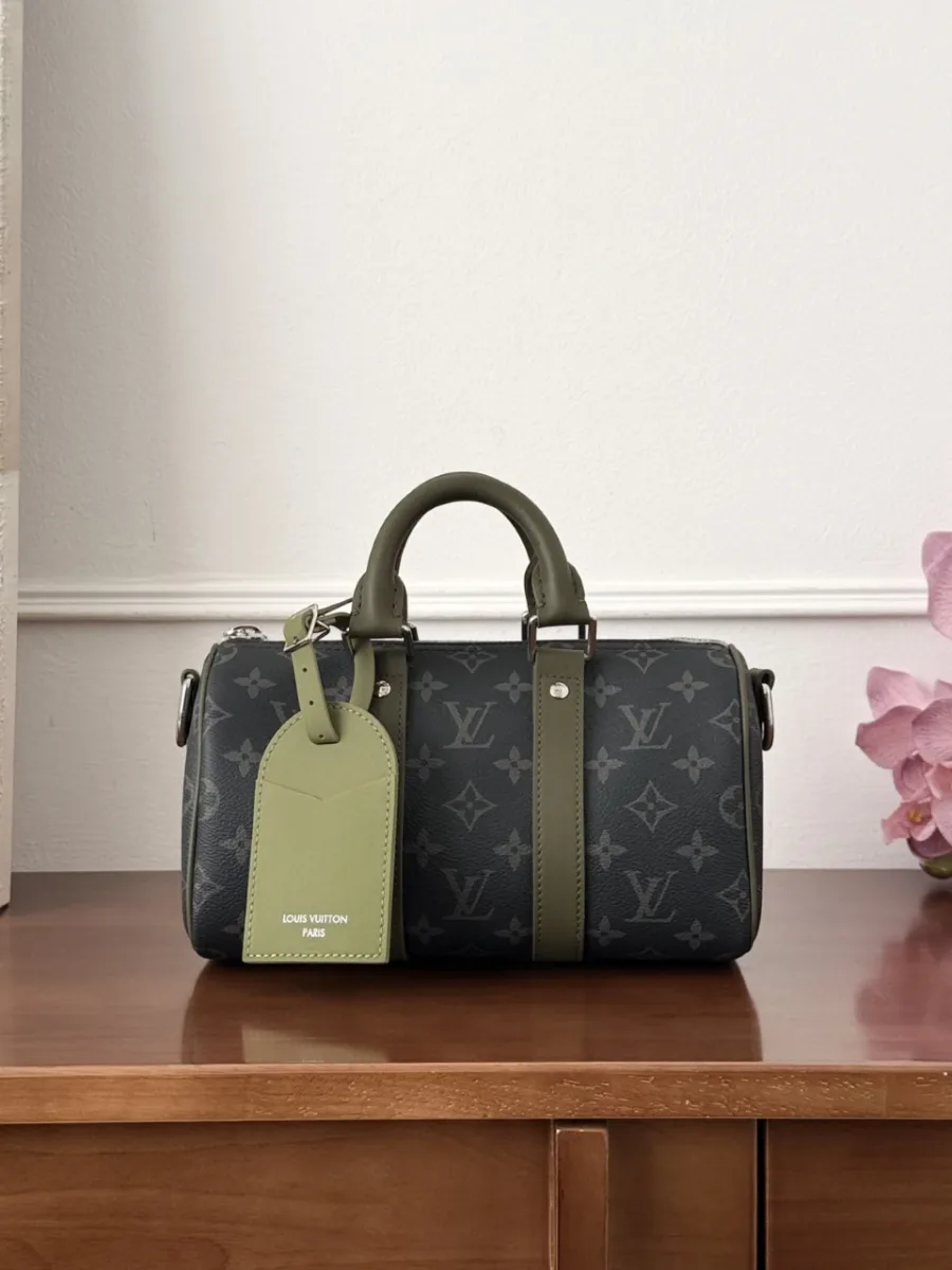 Сумка Louis Vuitton Keepall 25 из тёмной канвы с зелёной багажной биркой, вид спереди