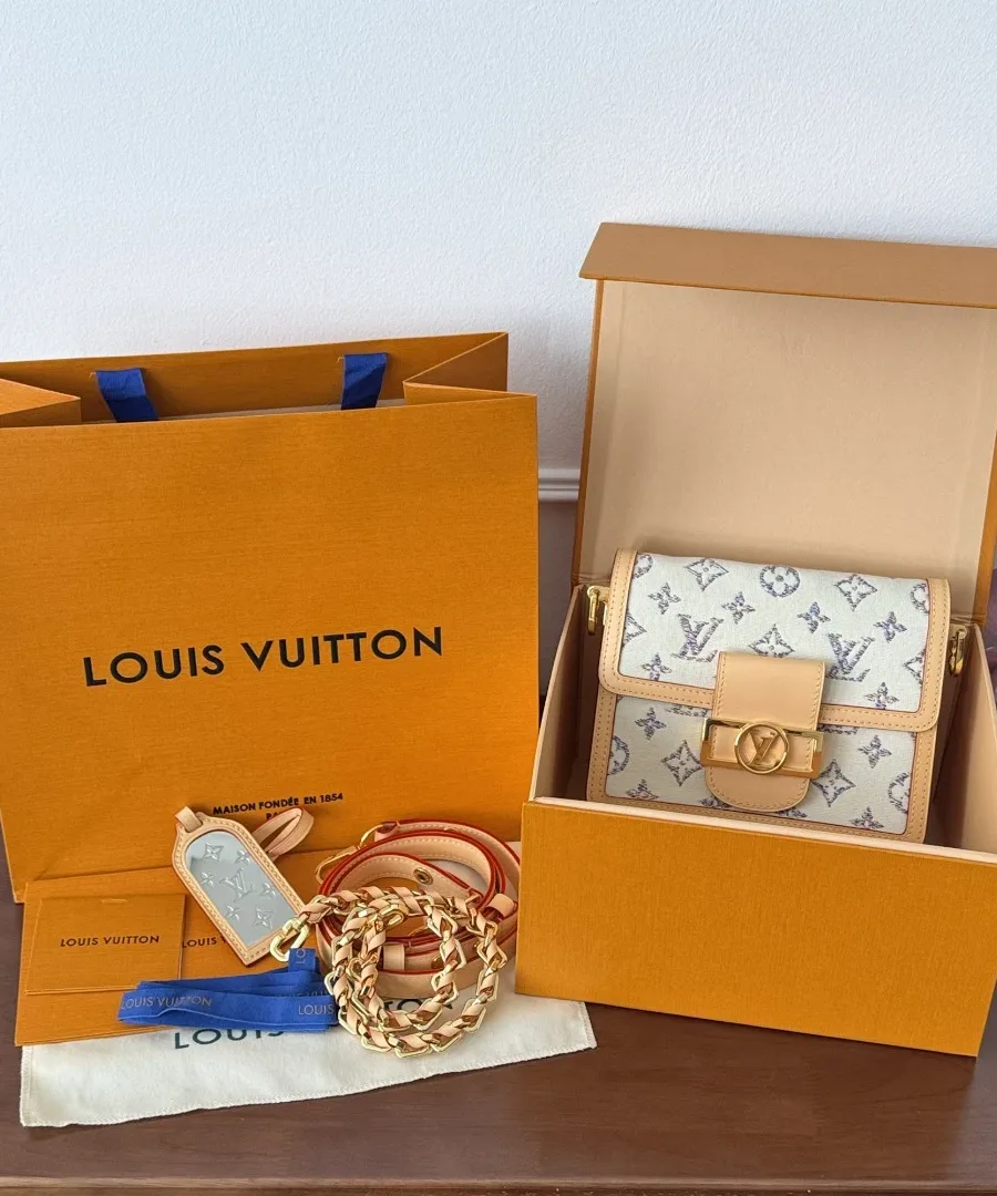 Сумка Louis Vuitton Dauphine Mini в фирменной коробке рядом с бумажным пакетом.