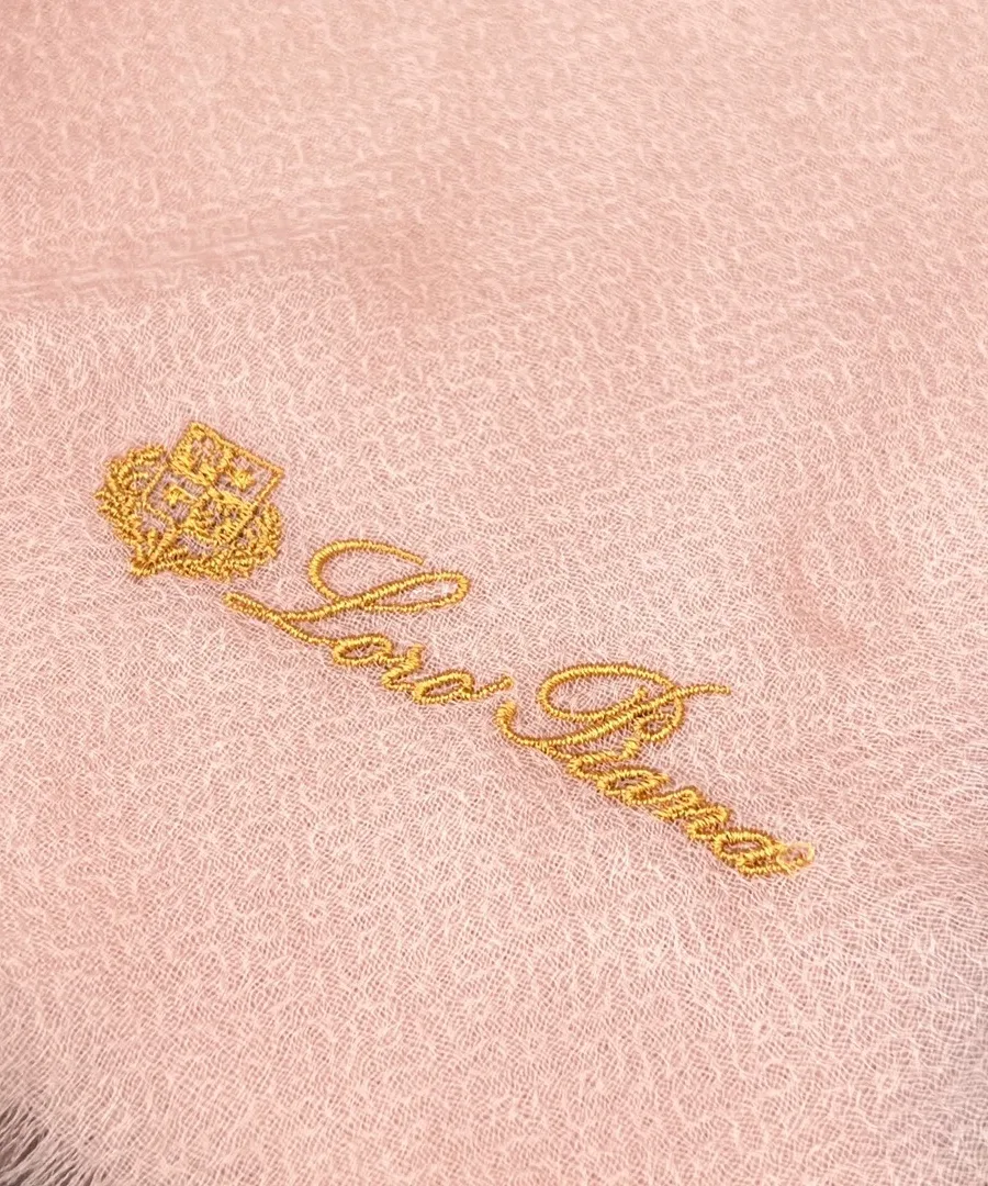 Золотистая вышивка логотипа Loro Piana на розовой ткани крупным планом