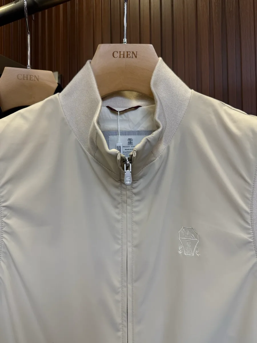 Бежевый пуховый жилет, крупный план верха, воротник-стойка в рубчик и вышитая эмблема