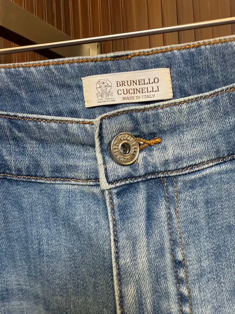 Металлическая пуговица на поясе джинсов и фирменная тканевая бирка Brunello Cucinelli