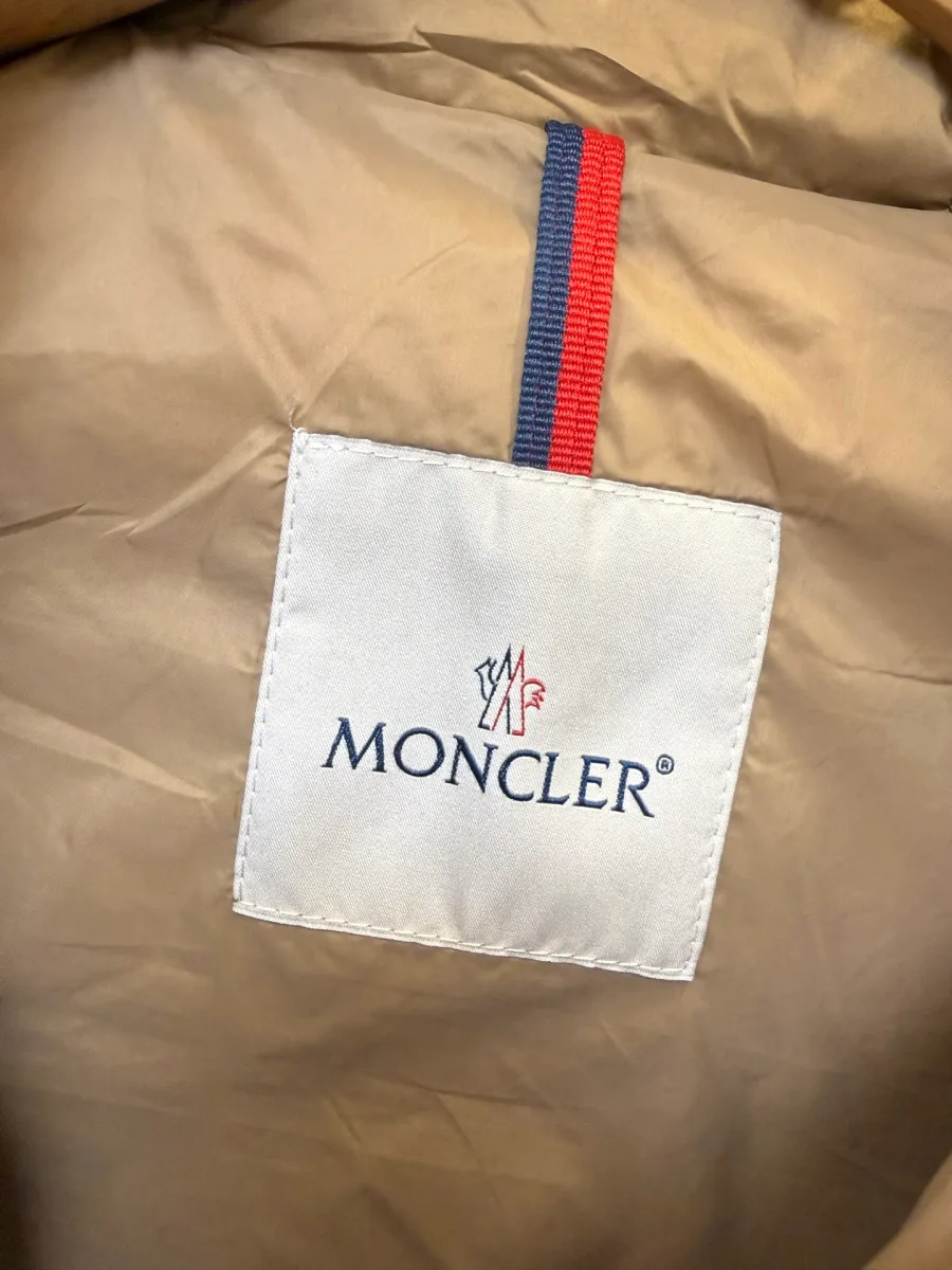 Фирменная бирка Moncler на внутренней части бежевого пуховика с трёхцветной текстильной петлёй