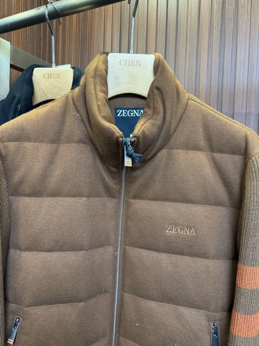 Воротник-стойка и вышитый логотип Zegna на груди коричневого пуховика, крупный план